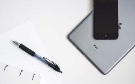 A phone on a tablet beside a notepad and pen